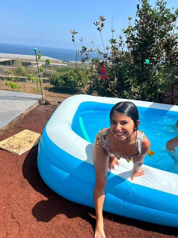Niña sonriente saliendo de la piscina infantil apoyada en el borde