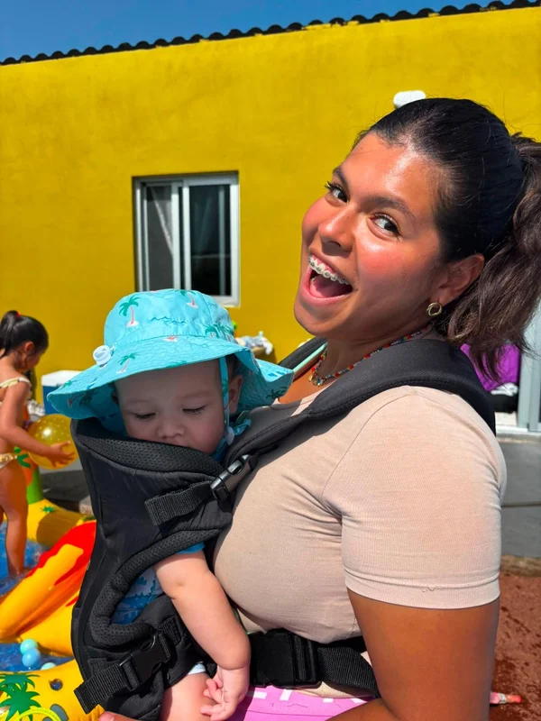 Madre o monitora llevando a un bebé sonriente en un portabebés
