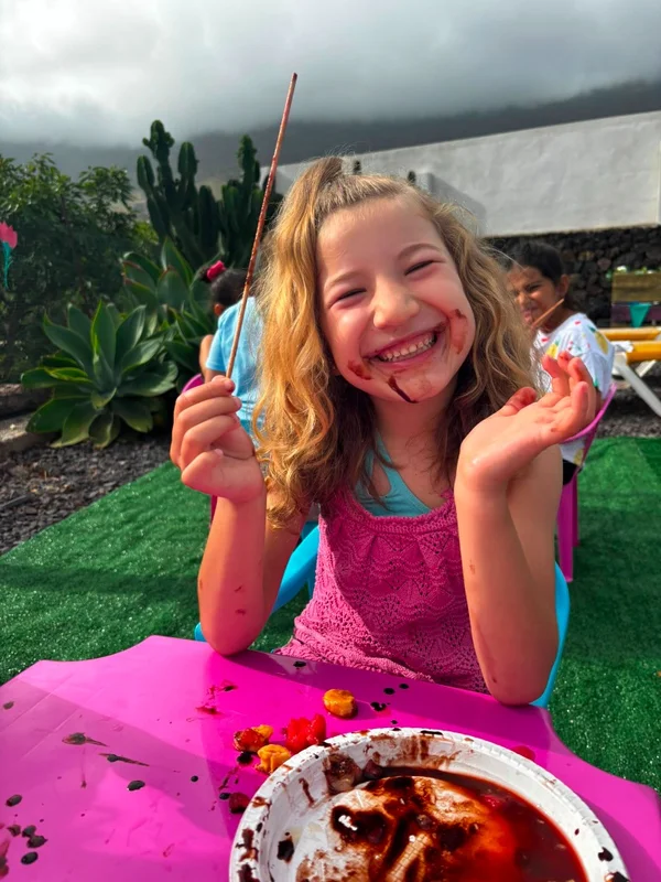 Niña rubia sonriente con la cara manchada de chocolate comiendo fresas