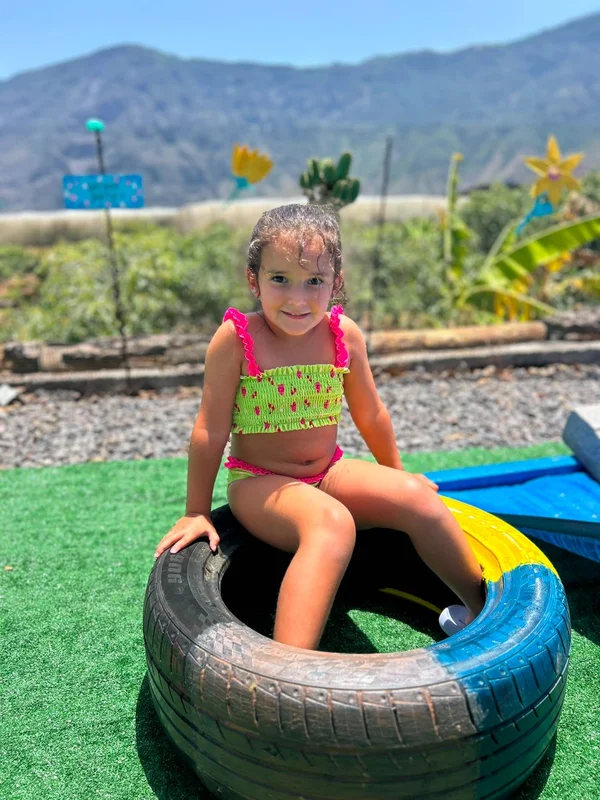 Niña con bañador verde y rosa sentada feliz en una rueda pintada en el jardín